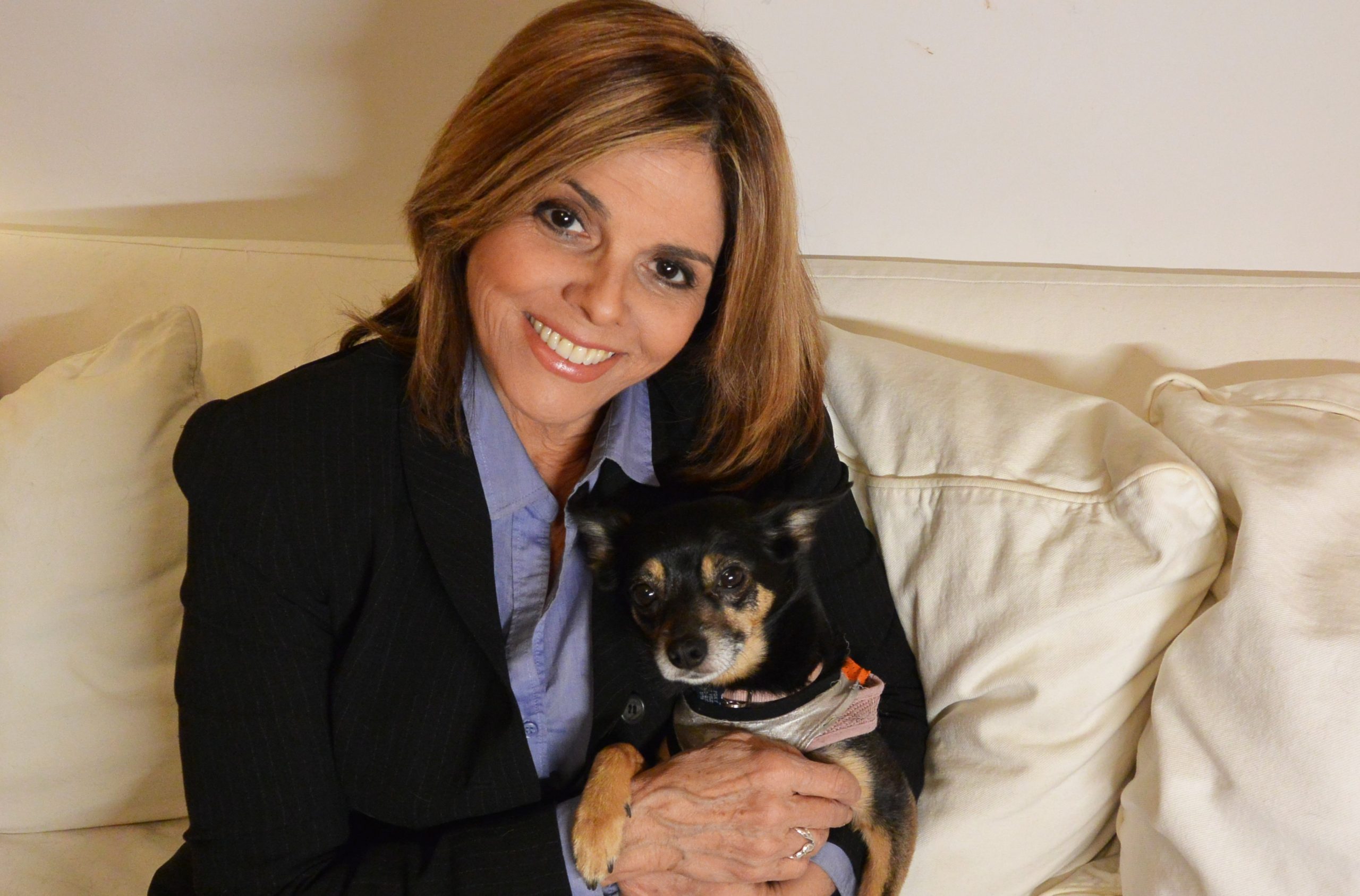 Smiling Latina woman holding dog sitting on white sofa