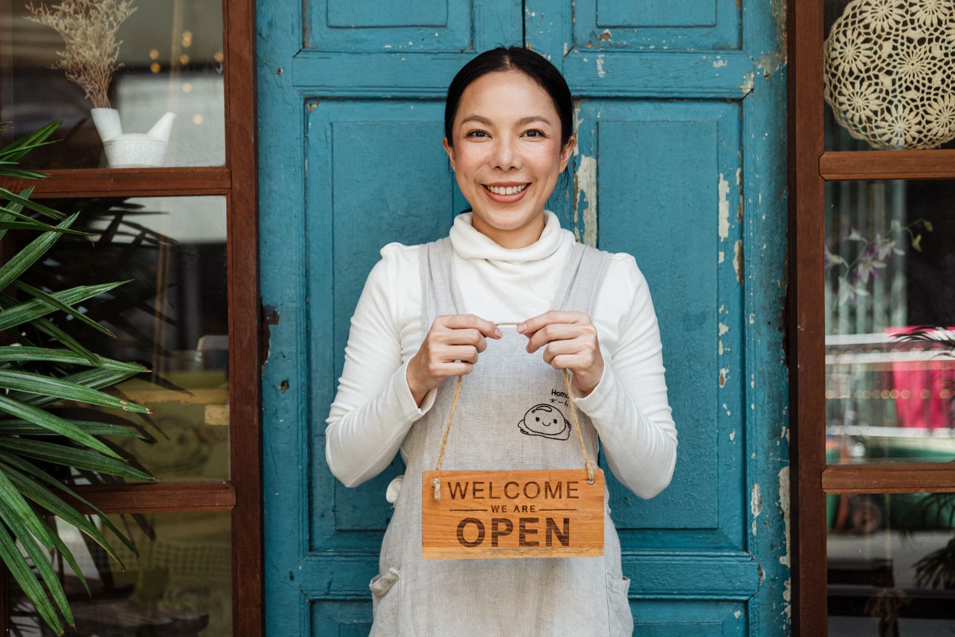 Woman in front of blue door holding welcome we are open sign