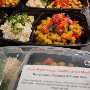 close up of ruby red vegan ready-to-eat meals mango curry chickpea and brown rice in black containers