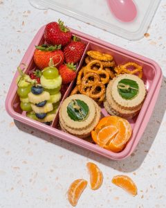 pink lunchbox with fruit pretzels grapes and orange slices