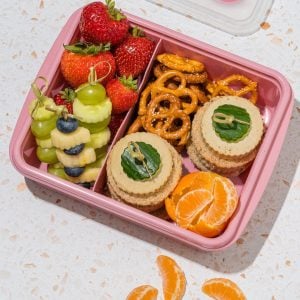 pink lunchbox with fruit pretzels grapes and orange slices