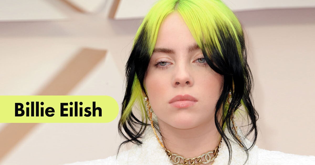 close up of billie eilish with neon yellow and black two tone hair wearing white jacket and chanel jewelery
