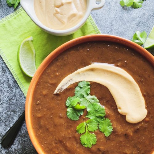instant pot black bean soup garnished with cilantro cream sauce and lime wedge