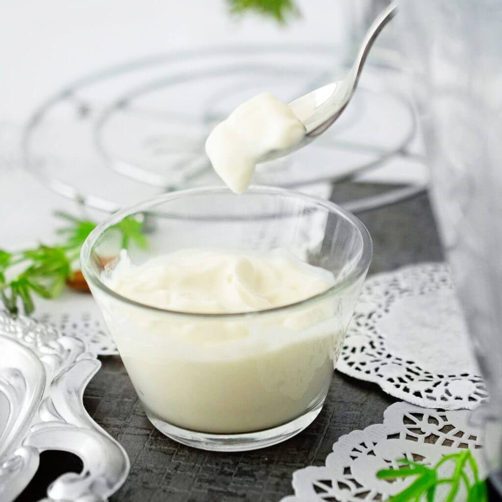 creamy vegan mayo being spooned out of small clear glass jar