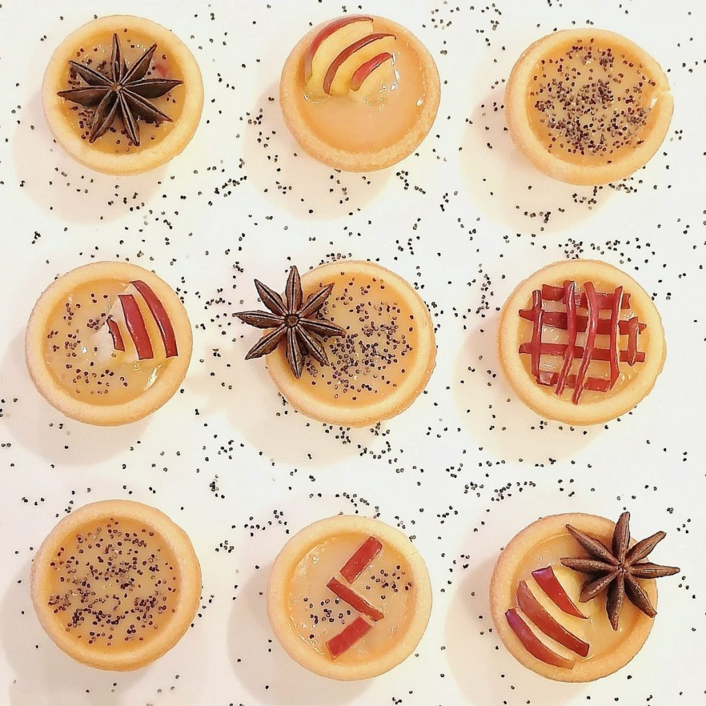 apple caramel tartlets arranged in rows of three garnished with apple peel chia and star anise