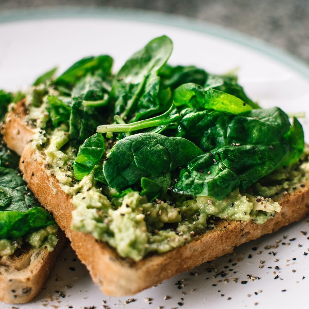mashed avocado on toast topped with baby spinach and black pepper