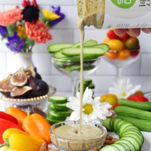 pouring jar of soco tahini and pesto vegetables slices with dip