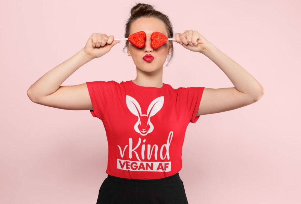 woman wearing red vKind t-shirt with puckered red lips and holding two heart shaped lollipops over her eyes