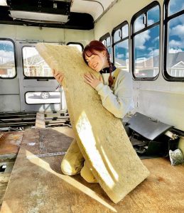 woman with braids and overalls hugs insulation in diy bus build