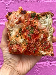Hand holding pizza against purple background