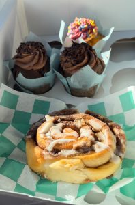 Cinnamon bun and two chocolate cupcakes and one multi color cupcake