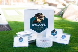 Various containers of Dylan's Dog Food in front of box on grass
