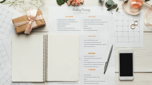 Wedding planning checklist laying on top of a calender page qith wedding rings, pen, smartphone and flower s